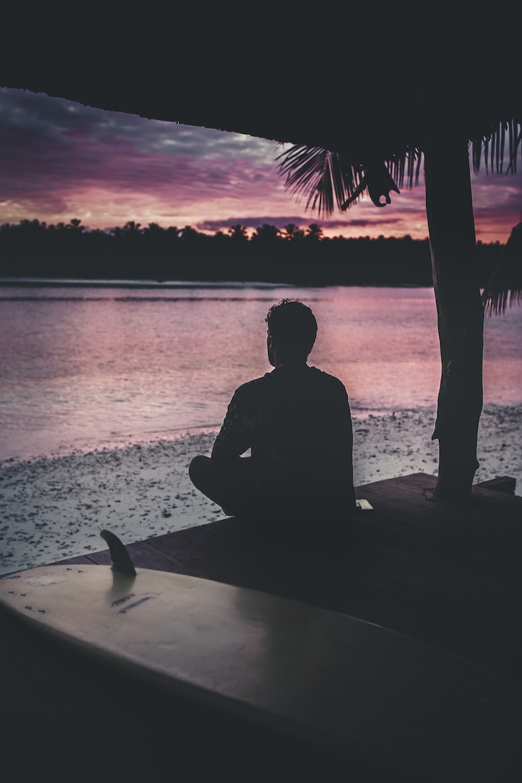 Foto gratuito silueta de una persona solitaria sentada junto al mar disfrutando de la hermosa vista del atardecer