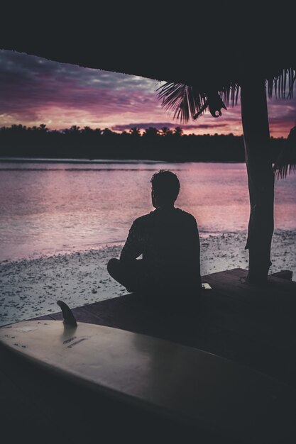 Silueta de una persona solitaria sentada junto al mar disfrutando de la hermosa vista del atardecer