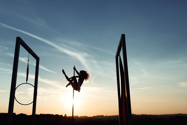 Silueta de sexy pole dancer actuando en el techo al atardecer