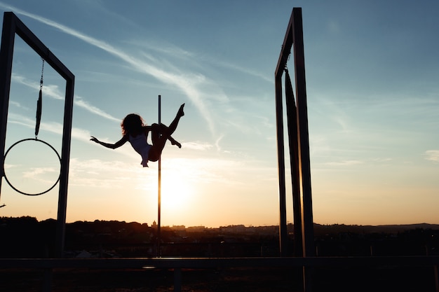 Silueta de sexy pole dancer actuando en el techo al atardecer