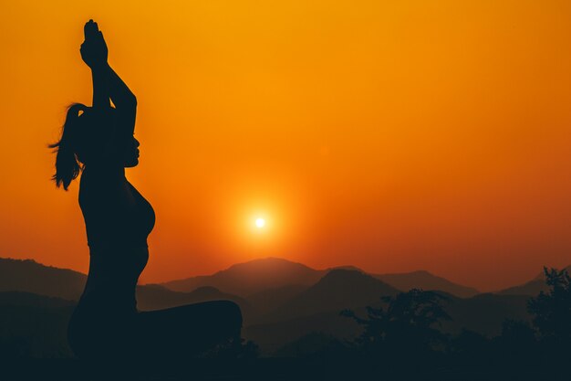 Silueta - Yoga girl está practicando en la azotea mientras se pone el sol.