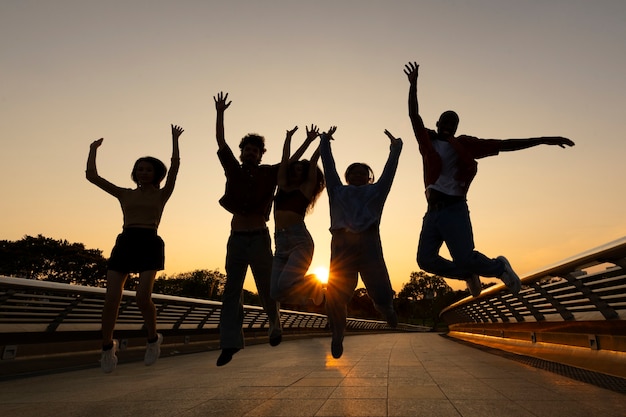 Foto gratuita siluetas de amigos de tiro completo saltando al atardecer