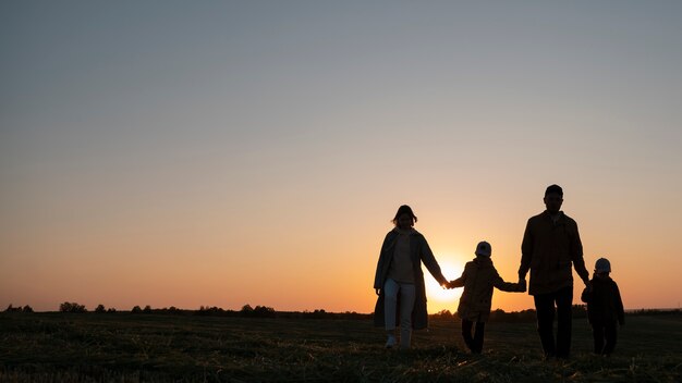 Siluetas familiares divirtiéndose al atardecer tiro completo