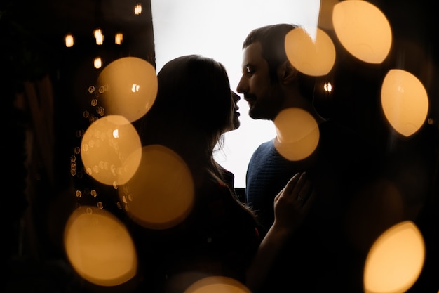 Siluetas de hombre y mujer rodeadas de luces navideñas amarillas.