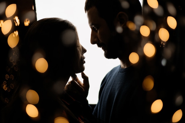 Siluetas de hombre y mujer rodeadas de luces navideñas amarillas.