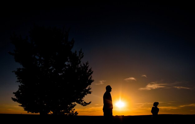 Siluetas de hombre y niña de pie en un campo antes de una puesta de sol