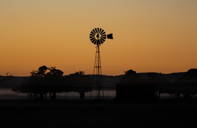 Foto gratuita siluetas de un molino de viento y árboles durante una increíble puesta de sol en la noche