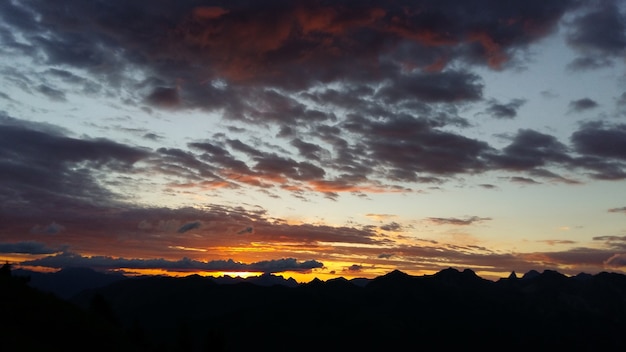 Siluetas de las montañas rocosas bajo un cielo nublado durante la puesta de sol en la noche
