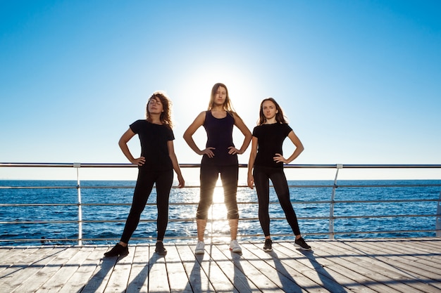 Siluetas de mujeres deportivas bailando zumba cerca del mar al amanecer