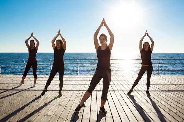 Siluetas de mujeres deportivas bailando zumba cerca del mar al amanecer