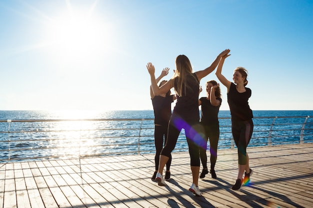 Siluetas de mujeres deportivas dando highfive cerca del mar al amanecer