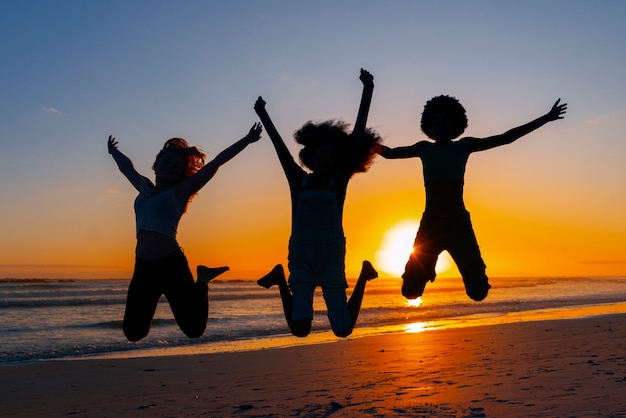 Foto gratuita siluetas de tiro completo de personas saltando al atardecer