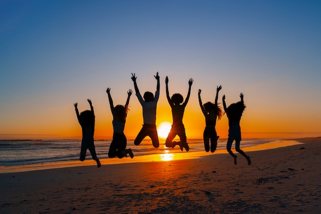 Siluetas de tiro completo de personas saltando al atardecer