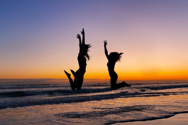 Foto gratuita siluetas de tiro completo de personas saltando al atardecer