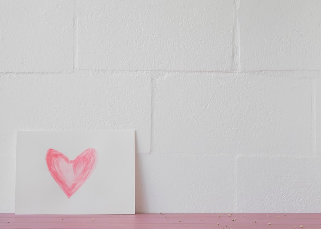 Símbolo del corazón en papel blanco cerca de la pared