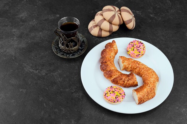 Simit, galletas de hojaldre, galletas de cacao y un vaso de té en la mesa negra.