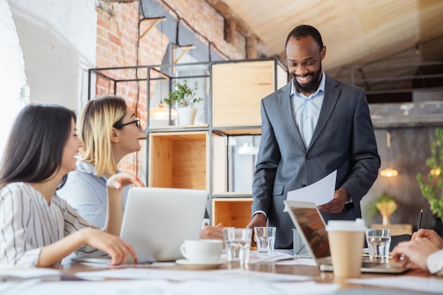 Simpático. Grupo diverso de compañeros de trabajo que tienen una discusión informal en la oficina. Ejecutivos durante una discusión amistosa, informes mensuales, reunión creativa. Concepto de negocio, finanzas, ocupación, trabajo.