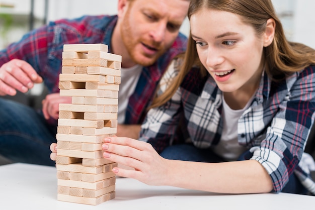 Sirva la mirada de la mujer joven sonriente que equilibra la torre del bloque de madera en la tabla blanca