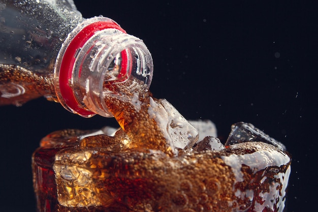 sirviendo una cola de una botella a un vaso lleno de hielo