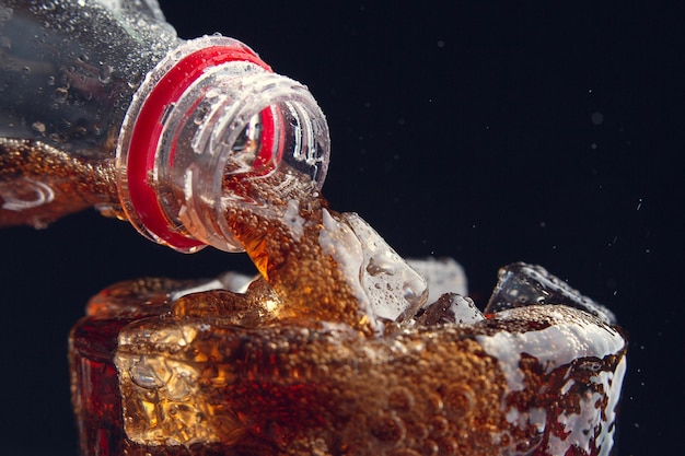 Sirviendo una Cola de una botella a un vaso lleno de hielo
