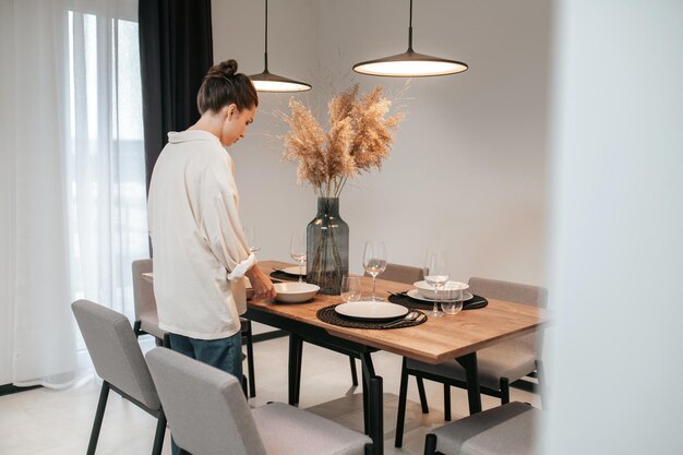 Sirviendo la mesa. Mujer joven con una camisa blanca poniendo platos en la mesa