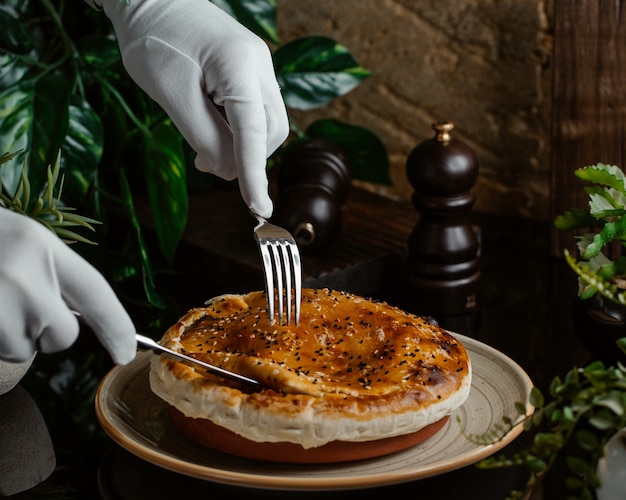 Un sirviente cortando cuidadosamente el pastel de carne dentro de un plato de cerámica