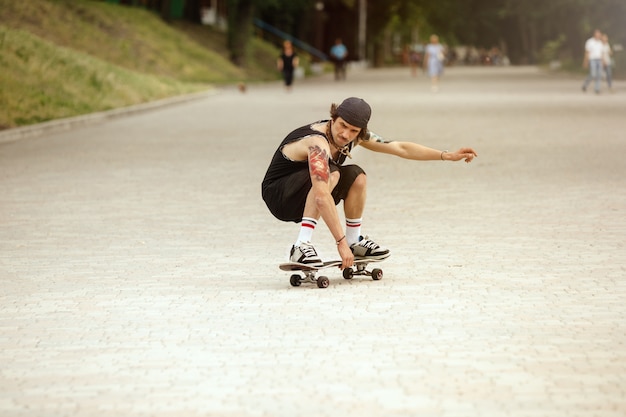 Skater haciendo un truco en la calle de la ciudad en un día nublado. Hombre joven en zapatillas y gorra de montar y hacer longboard sobre el asfalto. Concepto de actividad de ocio, deporte, extremo, afición y movimiento.