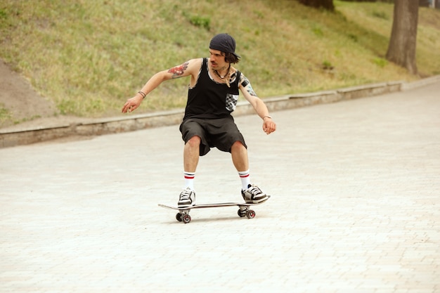 Skater haciendo un truco en la calle de la ciudad en un día nublado. Hombre joven en zapatillas y gorra de montar y hacer longboard sobre el asfalto. Concepto de actividad de ocio, deporte, extremo, afición y movimiento.