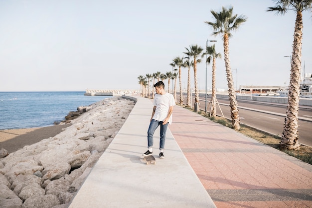 Skater masculino con un monopatín de pie junto al mar