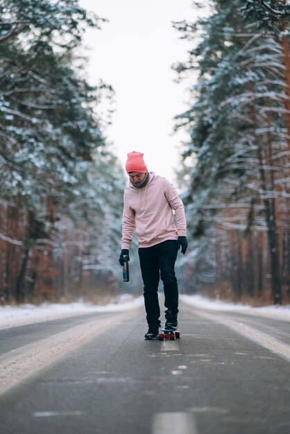 Skater de pie en la carretera en medio del bosque rodeado de nieve