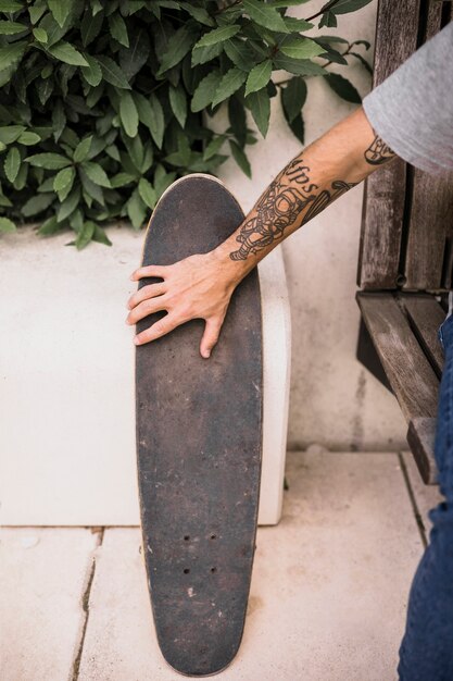 Skater con tatuaje en la mano sosteniendo patín