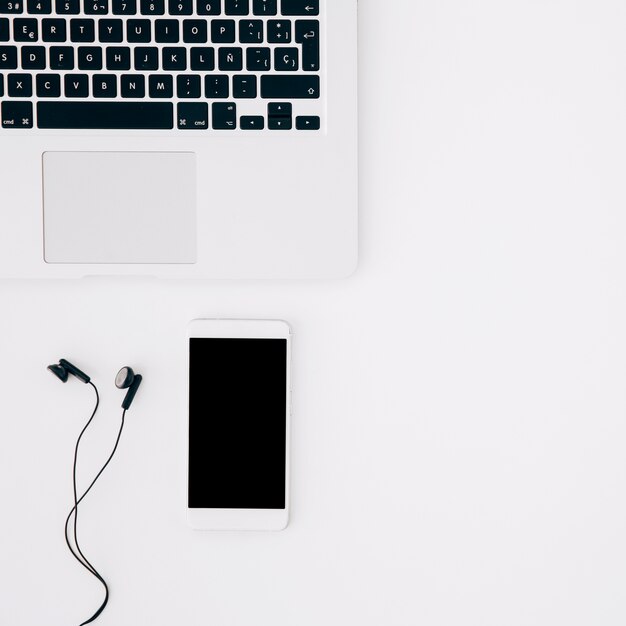 Smartphone y auricular con una computadora portátil abierta aislada sobre fondo blanco