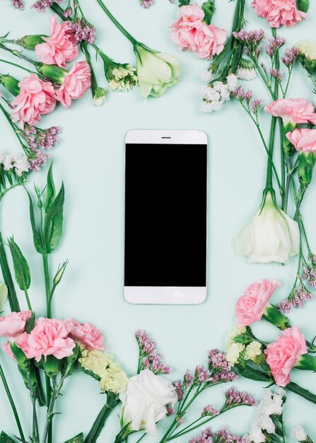 Smartphone en blanco rodeado de limonium fresco; claveles y flores de eustoma contra el fondo azul