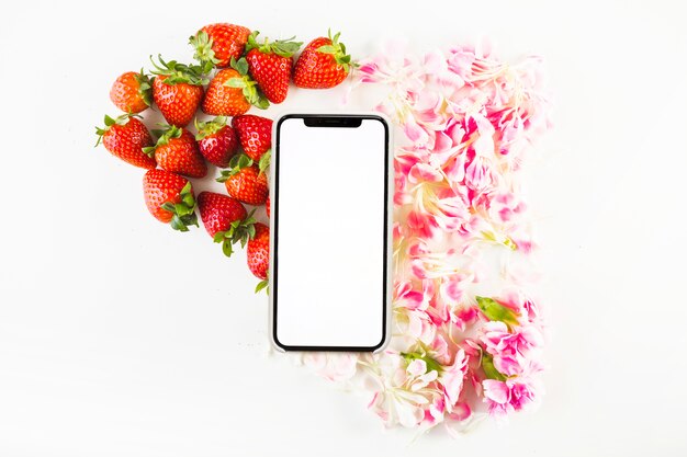 Smartphone cerca de fresas y pétalos