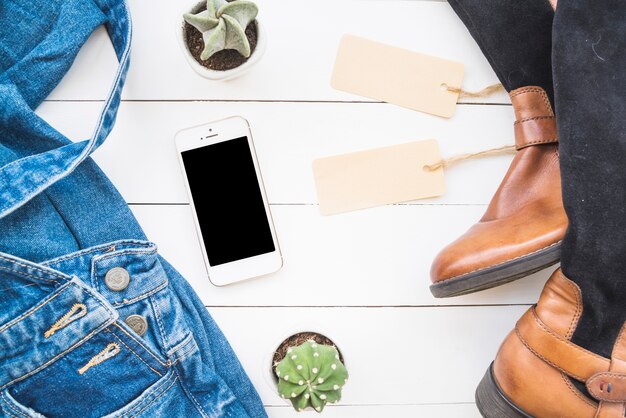 Smartphone cerca de tela de jean, botas altas con etiquetas y cactus.