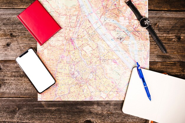 Smartphone, diario, libreta, mapa y reloj de pulsera en la mesa de madera