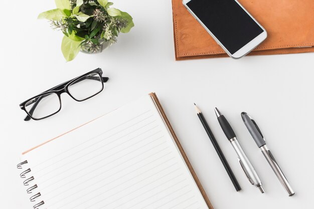 Smartphone y gafas cerca de papelería y planta