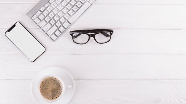 Smartphone, gafas, taza y teclado.