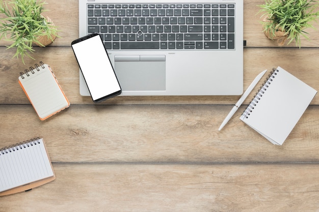Smartphone y laptop cerca de notebook en escritorio de madera