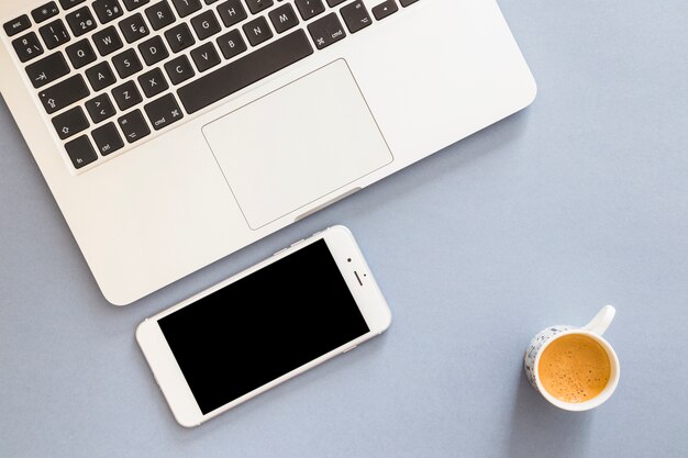 Smartphone con laptop y taza de café.