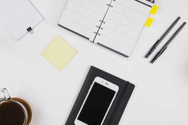 Smartphone con libreta y taza de café.