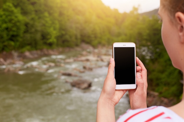 Smartphone en la mano de la mujer, el fotógrafo hace fotos de la hermosa naturaleza, pantalla en blanco en el dispositivo.
