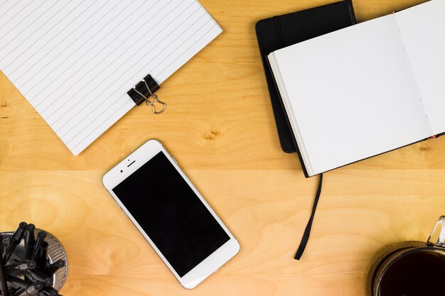 Smartphone con notebook y taza de café en la mesa