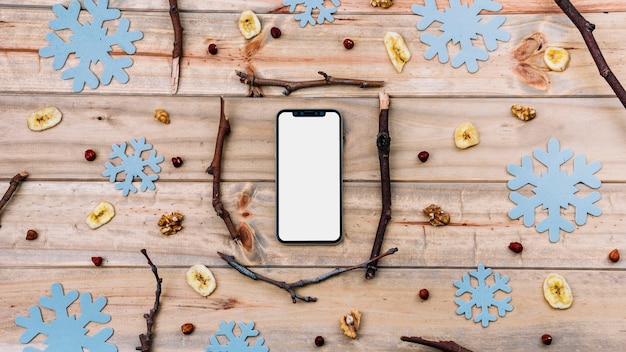 Smartphone entre ramitas y copos de nieve decorativos.