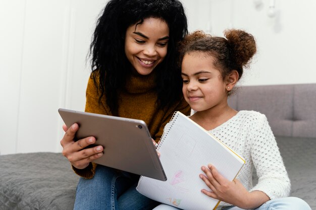 Smiley adolescente ayudando a hermana con tableta para escuela en línea