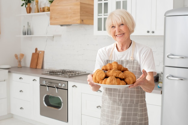 Smiley anciana sosteniendo un plato con cruasanes en la cocina