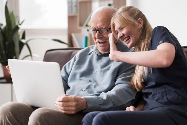 Smiley anciano y enfermera con una videollamada en la computadora portátil