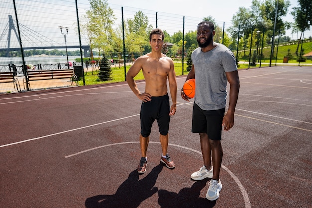 Foto gratuita smiley hombres de pie en la cancha de baloncesto tiro largo