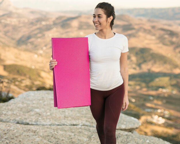 Smiley joven mujer sosteniendo estera de yoga