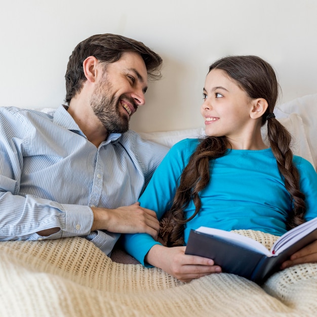 Smiley padre y niña en la cama leyendo